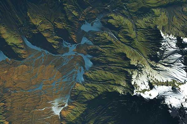 An aerial view of a map showing the landscape of a mountain region, with dark green and brown colors. White clouds are visible on the map, as well as blue water streams.  